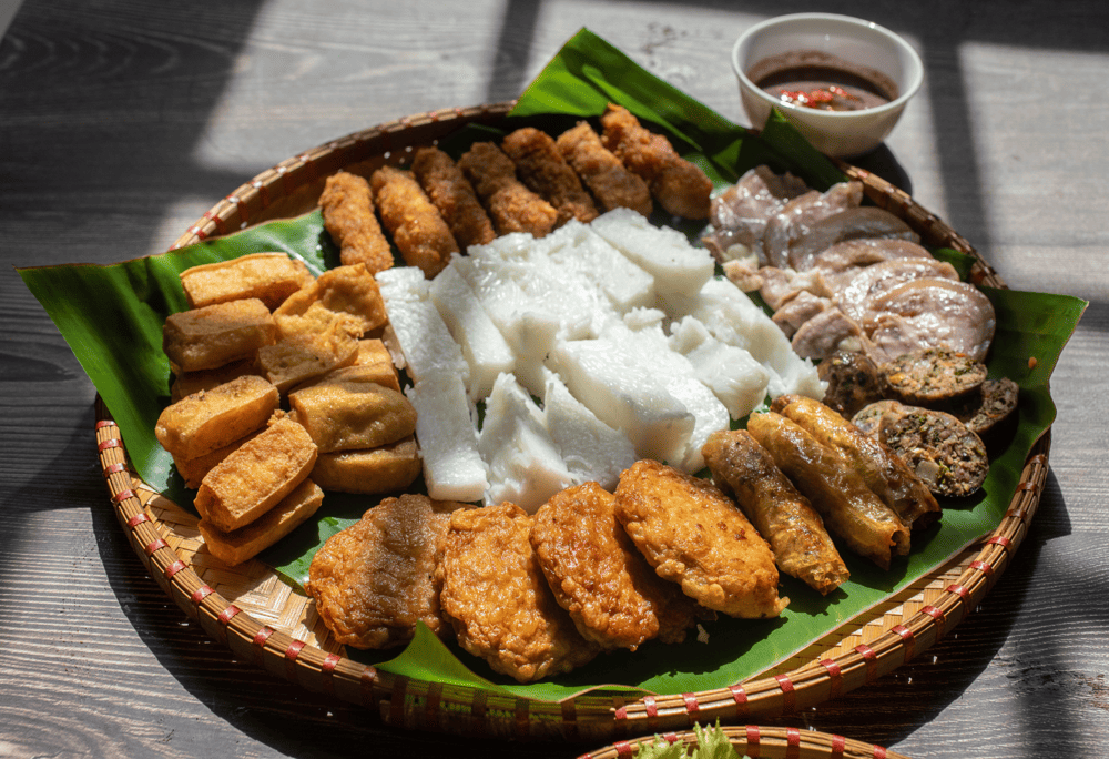 The dish, usually served on a round bamboo tray lined with banana leaves, features fresh noodles, fried tofu, boiled pork, herbs, and shrimp paste (Source: Canva)